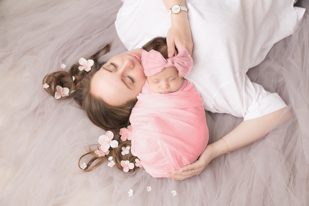 Newborn photography session hayley morris malvern studio baby wrapped and placed posed on her mum's shoulder with mum lying down on soft tulle. Flowers in mum's hair